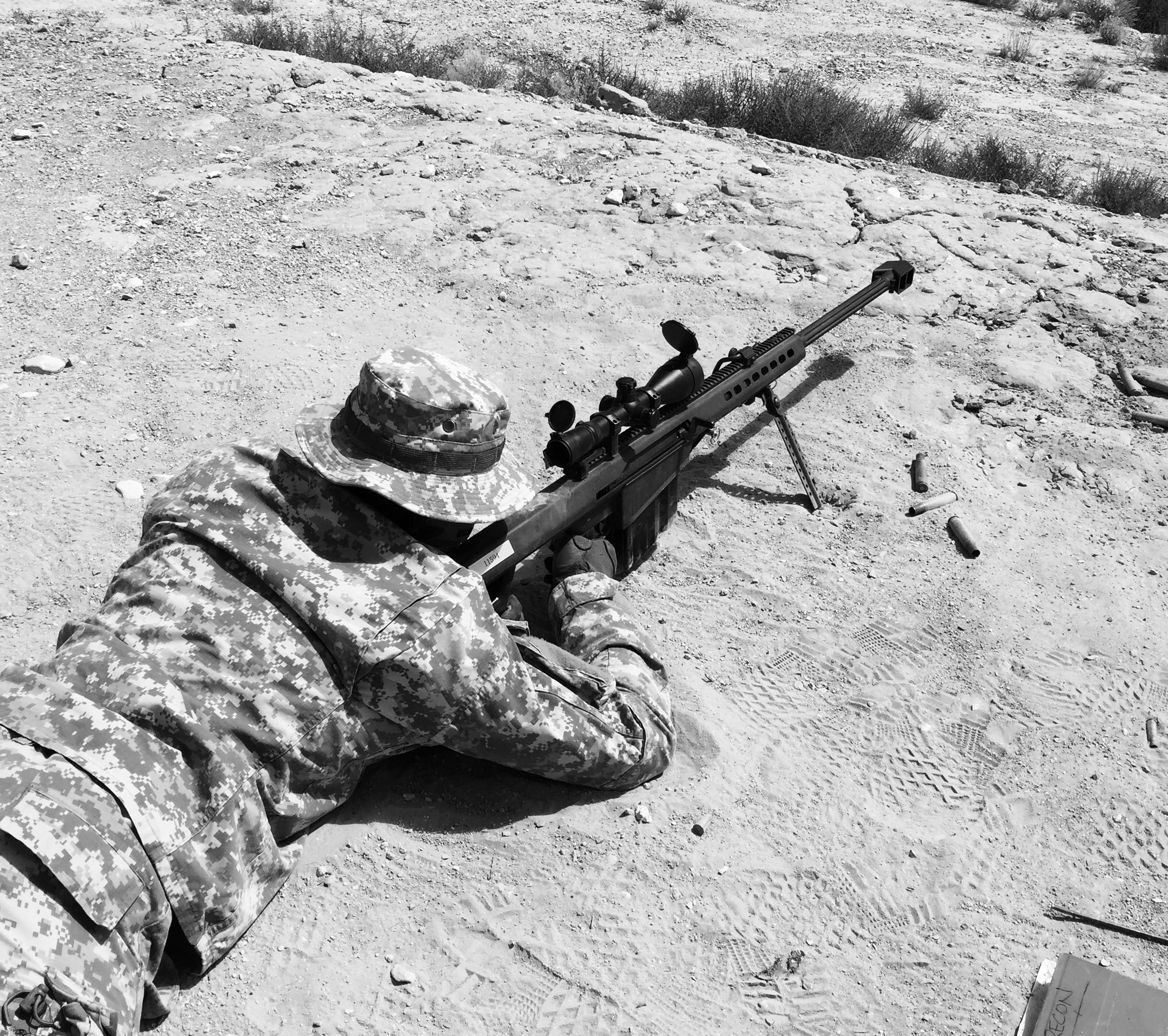 Lying in sand aiming with sniper rifle